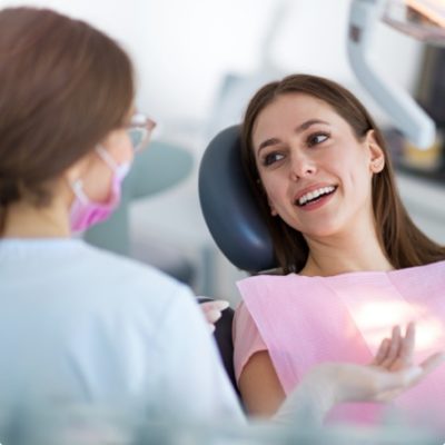 A young woman lays in a dentist chair, smiling at the dentist.