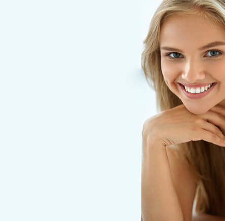 A woman with blonde hair smiles with her chin resting on the back of her hand.