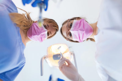 Two dental professionals lean over the camera, from the point of view of a patient on the table.