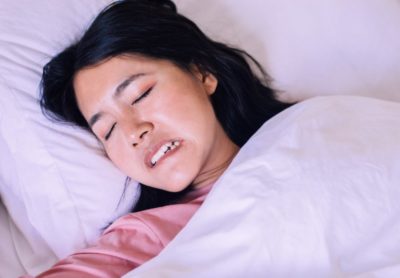 A woman lays in bed, grinding her teeth while sleeping.