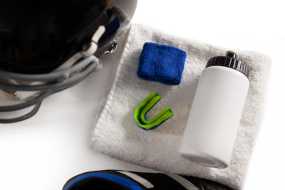 An overhead shot of a sports mouthguard, wristband, water bottle on a towel, and a football helmet.